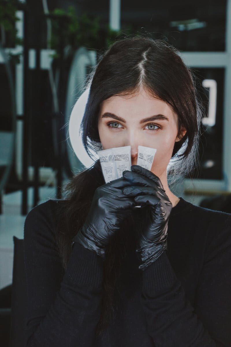 Portrait of an elegant woman with dark hair holding beauty products, wearing black gloves and shirt.